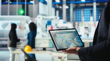 Fotovoltaik fabrikasındaki mühendis, güneş panelleri üreten robotların performansını gözden geçirmek için tablet üzerinde izleme yazılımı kullanıyor. Uzman, güneş santrali makinelerini incelemek için bir cihaz kullanıyor. Kamera. Yakın plan.