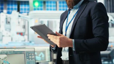 Fotovoltaik fabrikası mühendisi güneş panelleri verimliliğini arttıran bir tablet tutuyor. Güneş panelleri daha ucuz ve daha sürdürülebilir güneş çözümlerini araştıran fabrika işçisi üretiyor. Cihaz, kamera B kullanarak.