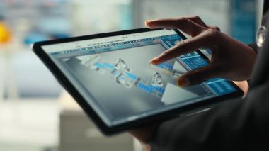 Fotovoltaik fabrikası uzmanı CAD uygulamasında tablet kullanarak üretim hatları tasarlıyor. Güneş panelleri fabrika teknisyeni, üretim planlarını optimize etmek için aygıt üzerinde simülasyon yazılımı kullanır, kamera B ise yakın plan