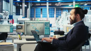 Yenilenebilir enerji fabrikasında çalışan robot kolların güneş panelleri yerleştirme performansını incelemek için dizüstü bilgisayar kullanıyor. Uzman, güneş hücrelerini taşıyıcı bantlara yerleştiren makineleri inceliyor. Kamera A