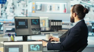 Robot kollarının performansını izlemek için PC kullanan Photovoltaics fabrika işçisi güneş panellerini montaj hatlarına yerleştiriyor. Bilgisayar masasında uzman, ekrana bakıyor, güneş santrali makinelerini inceliyor, kamera B