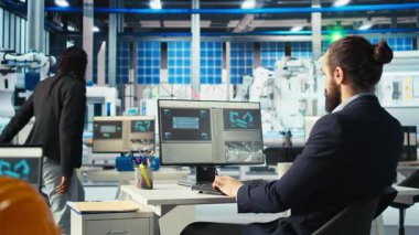 Robot kollarının performansını izlemek için PC kullanan Photovoltaics fabrika işçisi güneş panellerini montaj hatlarına yerleştiriyor. Bilgisayar masasında uzman, ekrana bakıyor, güneş santrali makinelerini inceliyor, kamera A