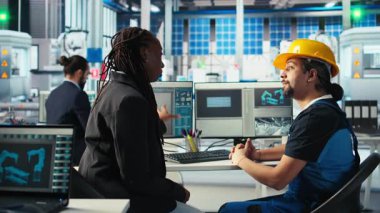 Fotovoltaik fabrika işçisi bir kadınla sistem performansı hakkında konuşuyor. Güneş panelleri üretim tesisi Afro-Amerikan yöneticisi mühendisle enerji üretimi ve kamera A hakkında sohbet ediyor.