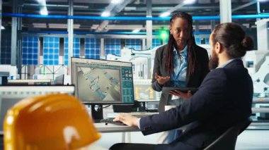 Fotovoltaik fabrikası müdürü ve iş arkadaşı beyin fırtınası, güç üretimini maksimuma çıkarmak için sistem parametrelerini ayarlıyor. Adam iş arkadaşıyla konuşuyor, güneş paneli santralinde enerji kaynağını optimize ediyor, kamera A