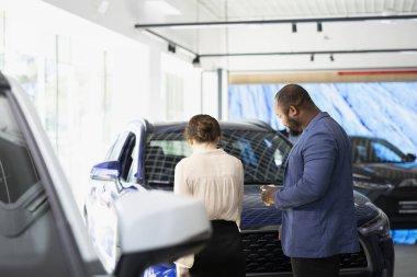 Galeride araba almak isteyen bir çift, arabaların durumunu değerlendiriyor. Galerideki müşteriler otomobilleri birlikte analiz ediyor, satın almak için ikna edici sebepler arıyorlar.