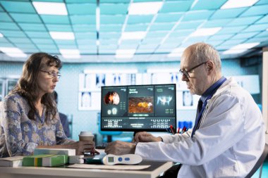 Kıdemli kadın, doktoruyla birlikte teşhis sonuçlarını kabinede değerlendiriyor. Hastasına doğru sonuçları vermek için ileri teknoloji aletleri kullanıyor. Tıp endüstrisinde bakım yönetimi.