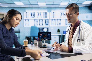 Hintli uzman, test sonuçlarını, muayenehanedeki bir erkek hastayla birlikte, genç bir adamı kontrol ederken tarama yaparak açıklıyor. Sigorta konusunda sağlık hizmetleri.