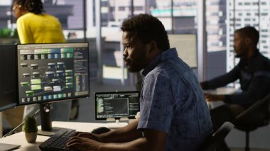 Bilgisayar bilimcisi, çalışma alanında dolaştıktan sonra PC kullanarak yazılım hata ayıklama işlemine devam ediyor. Ofiste tabletle yürüyen bir adam, bilgisayar ve kamera A kullanarak kodlama sorunlarını düzeltiyor.