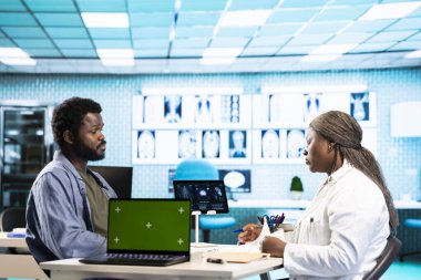 Afro-Amerikalı genç bir adam, sağlık uzmanına mankenin yanındaki tavsiyeyi soruyor, sağlık kontrolünde tıbbi kayıtları birlikte analiz ediyor. Hasta hastayla doktor toplantısı..