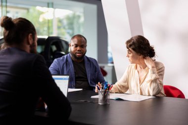 Araba galerisi satış danışmanı şartları kabul ettikten sonra müşterilere doldurmaları için satın alma formları veriyor. Showroom çalışanı karı koca için satış sözleşmesi imzalıyor.