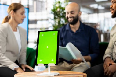 Ofisteki gülümseyen çok ırklı çalışanlar iş ortaklarıyla olan ilişkilerini sürdürüyorlar, yeşil ekran tabletindeki ölçülere bakıyorlar. Hisse sahiplerinin verilerini modelleme aygıtında gösteren çeşitli yöneticiler