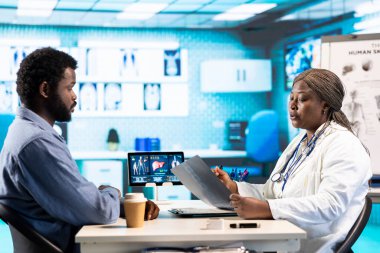 Genel pratisyen hekim, erkek hasta kontrolünde röntgen görüntülemesini inceliyor. İyileşmesini sağlamak için ona profesyonel uzmanlık öneriyor. Sıhhiye ofiste bir adamla tarama yapıyor..