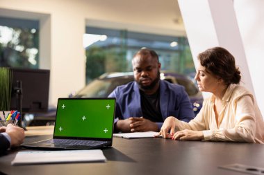 İzole edilmiş ekran dizüstü bilgisayar, pazarlık fiyatı ve anlaşmayı sağlamlaştırmak için ekstra araba özellikleri kullanarak satış temsilciliği yapıyor. Temsilci, krom anahtar defteri kullanarak tereddütlü müşterileri araç almaya ikna ediyor