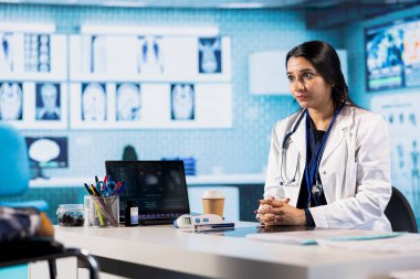 Hintli pratisyen doktor, tekerlekli sandalye kullanıcısı hastasını röntgen sonuçlarıyla ilgili konuşmak için selamlıyor. Kadın doktor sağlık sigortası ve sağlık sigortası altında tarama yapıyor..