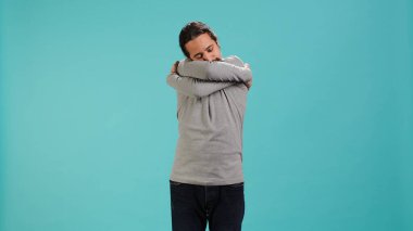 Stüdyoda duran bir adamın portresi, stüdyo arka planında izole edilmiş rahatlık ve kendini sevme jesti ile kendine sarılıyor. Neşeli insan kendini kabul ediyor, kendini kucaklıyor, kamera A.