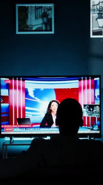 Dikey Video Rahatlatıcı kişi gece televizyonda flaş haber izliyor, oturma odasında kanepede dinleniyor ve televizyon programı izliyor. Küresel ağda medya bilgilerini dinleyen genç yetişkin