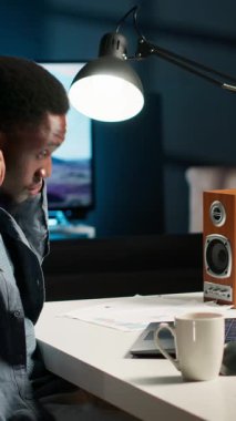 Dikey Video Afrikalı Amerikalı uzman aylık dengeyi kulaklıkla kapatıyor, en sevdiği podcast 'i dinlerken uzaktan çalışıyor. Masrafları ve sigortaları evden yönetmek