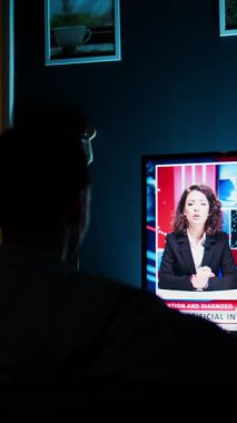 Dikey Video Endişeli Vatandaş TV 'de son dakika haberleri programını izliyor, haber spikerinin dünya çapında son olayları açıklamasını dinliyor. Genç yetişkin günlük medya manşetlerini takip ediyor. Kamera A.