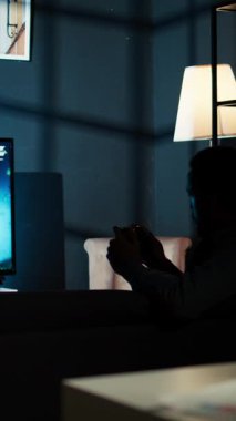 Dikey Video Siyah Yetişkin Oyuncu, başarılı oyun turundan sonra kendini yetenekli ve neşeli hissederek, gece online nişancı turnuvasını kazanıyor. Genç adam video oyunu oynuyor, evde eğleniyor.