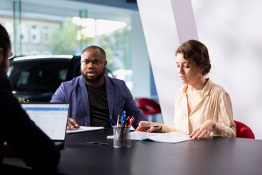 Araba galerisindeki müşteriler test sürüşüne çıkmadan önce otomobil kataloğuna göz atıyorlar, özellikleri ve fiyatlandırma seçeneklerini kontrol ediyorlar. Müşteriler yatırım yapmadan önce araç modellerini karşılaştırıyorlar