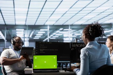 Sunucu çiftliğindeki bir grup programcı yeşil ekran laptopunu kullanarak yanlış yapılandırmaları arıyor. Afrika kökenli Amerikalı bilişim uzmanları veri merkezindeki hataları kroma anahtar defteriyle onarıyor