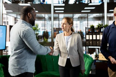 İş adayı ile görüşme yapan, el sıkışan, sorular soran ve şirket geçmişini sunan bir muhabir. İnsan kaynakları çalışanı açık pozisyon için röportaj yapıyor.