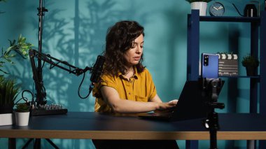 İçerik üreticisi canlı yayın yapıyor, hayranlarla son zamanlardaki haber başlıkları hakkında konuşuyor, dizüstü bilgisayardan okuyor. Abonelerle sohbet eden, not defteri cihazıyla ilgili bilgi sunan kadın, kamera B