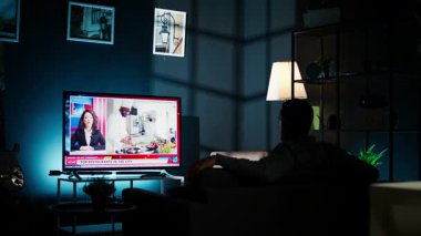 Geceleri, genç adam TV 'deki son manşetleri takip ediyor oturma odasındaki kanepede dinleniyor, haber programını izliyor. Uluslararası kanaldaki kişi yayınlanan bilgilere dikkat ediyor. Kamera A.