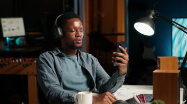 Afro-Amerikalı adam el sallıyor ve kentsel dairesinden bir web toplantısına katılıyor. Erkek serbest çalışan, video konferans görüşmesi için kablosuz bağlantıyı kullanarak iş arkadaşlarıyla uzaktan görüşüyor. Kamera B.