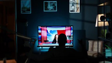 Geceleri televizyonda son dakika haberleri seyreden, oturma odasında kanepede dinlenen ve televizyon izleyen rahat bir insan. Global ağda medya bilgilerini dinleyen genç bir yetişkin. Kamera A.