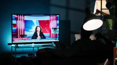 Geceleri televizyonda son dakika haberleri seyreden, oturma odasında kanepede dinlenen ve televizyon izleyen rahat bir insan. Global ağda medya bilgilerini dinleyen genç bir yetişkin. Kamera B.