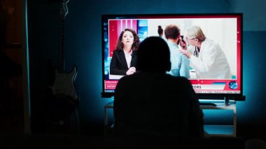 Akıllı TV 'de haber başlıklarını okuyan meraklı izleyiciler, koltukta oturup gazetecilerin son zamanlardaki küresel olaylarını dinliyorlar. Günlük haber başlıklarını izleyen adam, televizyon içeriği. Kamera B.