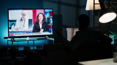 Geceleri, genç adam TV 'deki son manşetleri takip ediyor oturma odasındaki kanepede dinleniyor, haber programını izliyor. Uluslararası kanaldaki kişi yayınlanan bilgilere dikkat ediyor. Kamera B.