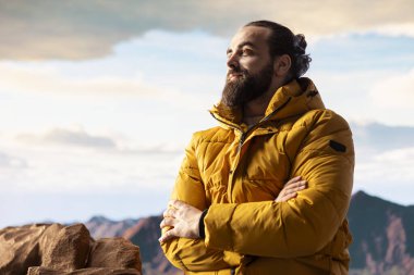 Bir dağ zirvesinde gezgin temiz havayı ve panoramik manzarayı içine çekiyor. Dağcı doğa aşığı engebeli tepelerin, engin gökyüzünün, maceranın ve gezinin çarpıcı manzarasına hayran kalır..