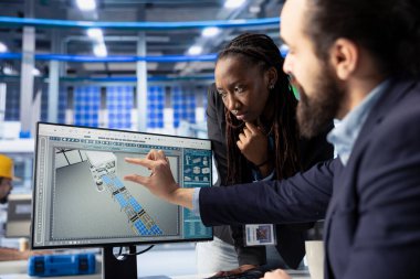 Güneş panelleri fabrika iş ortaklarını bilgisayarda enerji tüketimine bakıyor. PC kullanarak imalat kaynaklarını yöneten fotovoltaik tesisinde çalışan kadın ve erkek.