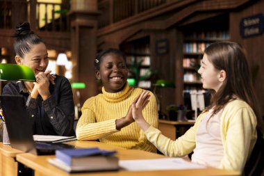 Özel dersler sırasında kütüphanede öğretmenle beşlik çakıp takım ödevlerini bitiren mutlu liseli kızlar. İlkokul öğrencileri akademik ilerlemeden memnun..