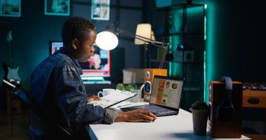 Girişimci evde çalışıyor, dizüstü bilgisayar kullanıyor, kağıda notlar yazıyor. Kişisel apartman ofisindeki uzaktan çalışan, not defterine önemli bilgiler kaydeden, istatistik tablolarına bakan, kamera B