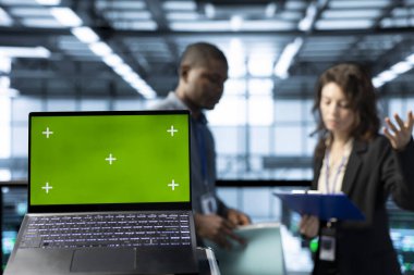 Veri merkezi teknisyenlerinin önündeki yeşil ekran dizüstü bilgisayarı bulanık arka planda enerji kullanımını ayarlıyor, UPS yapılandırmalarını denetliyor, sürdürülebilir altyapıyı destekliyor