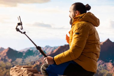 İçerik yaratıcısı, dağlardaki bir vlogu çevrimiçi izleyicisiyle yürüyüş yolculuğunu paylaşırken kaydediyor. Erkek kâşif her zaman dengeleyici bir tripoda monte edilmiş akıllı bir telefonla bağlanır..
