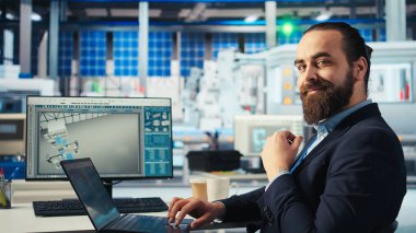 Yenilenebilir enerji fabrikasında çalışan robot kolların güneş panelleri yerleştirme performansını incelemek için dizüstü bilgisayar kullanıyor. Uzman, güneş hücrelerini taşıyıcı bantlara yerleştiren makineleri inceliyor. Kamera A