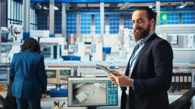 Fotovoltaik fabrikası mühendisi güneş panelleri verimliliğini arttıran bir tablet tutuyor. Güneş panelleri daha ucuz ve daha sürdürülebilir güneş çözümlerini araştıran fabrika işçisi üretiyor. Cihaz, kamera A kullanarak.