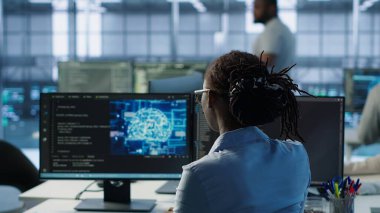 Sunucu merkezindeki bilgisayarda yazan mühendis, veri merkezi enerji tüketimini yapay zeka yazılımı kullanarak izliyor. Teknisyen sunucu odasındaki sırt çantalarını yapay zeka teknolojisi ve kamera A kullanarak inceliyor.