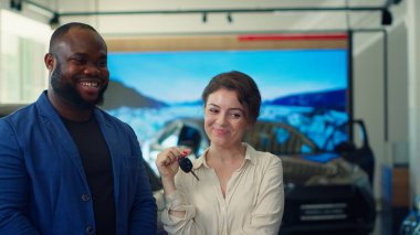 Kapanış anlaşmasını kutlayan ve galeriden araba alan neşeli müşterilerin portresi araç anahtarlarını gururla sallıyor. Gülümseyen eş ve koca otomobilden memnun, kamera A