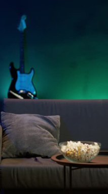 Dikey Videocu eve geliyor, kanepede dinleniyor, TV 'de gösterilen filmleri izlerken patlamış mısır yiyor. Apartmana giren, abur cubur yiyen ve neon ışıklı oturma odasında yayın yapan kişi, kamera A