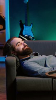 Dikey video iyimser ev sahibi kanepeye uzanıyor, TV 'de film izliyor, komik sahnelerle eğleniyor. Ev sinemasında eğlenen, iyi filmler izleyen, patlamış mısır yiyen, kamera yiyen mutlu bir adam.