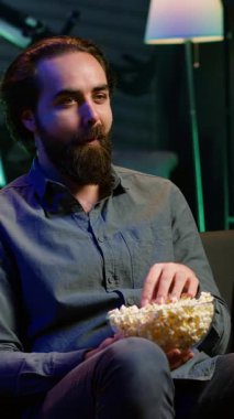 Dikey video, TV 'de oturup aboneliğe dayalı komedi dizisini abone olmak, patlamış mısırın tadını çıkarmak için kullanmaktan keyif alan biri. Televizyondaki komik şovlara gülen, abur cubur yiyen adam.