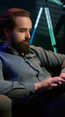 Evde televizyon izlerken dizüstü bilgisayara e-posta yazan dikey video telgrafçısı. Evden çalışan, rahat bir dairede çalışan, not defterine yazan, uzaktan kumandayla televizyonu açan bir çalışan.