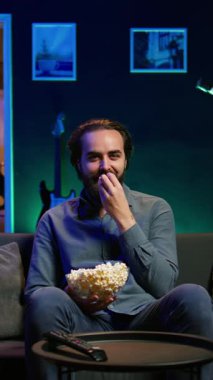 Dikey video, TV 'de oturup aboneliğe dayalı komedi dizisini abone olmak, patlamış mısırın tadını çıkarmak için kullanmaktan keyif alan biri. Televizyondaki komik şovlara gülen, abur cubur yiyen adam.
