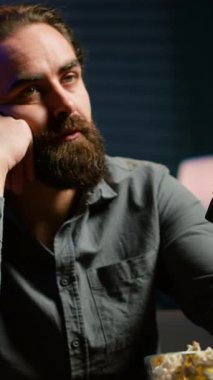 Dikey video sıkıntısı çeken adam evde kanepede dinleniyor, patlamış mısır yiyor ve TV 'de film seyrediyor. Tembel insan abur cubur yiyor ve RGB 'nin aydınlattığı oturma odasında televizyon kanallarında zaplıyor.