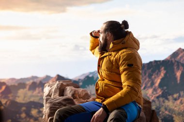 Sıcak giysili bir gezgin, yüksek irtifa keşifleriyle gelen özgürlük hissini hissederek, geniş bir dağ manzarası izler. Doğa aşığı temiz havayı ve vahşi doğayı sever..